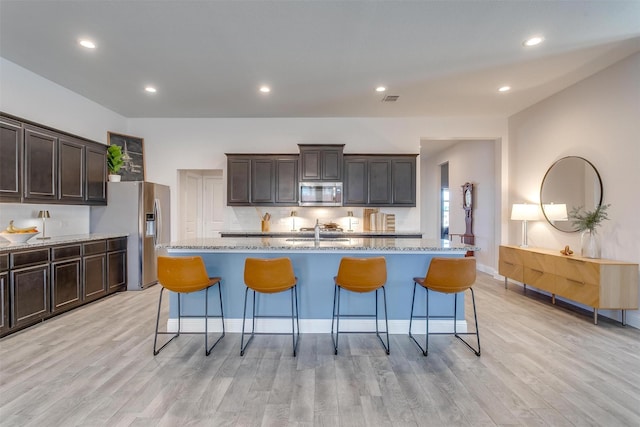 kitchen with light wood-type flooring, a kitchen bar, light stone counters, and stainless steel appliances