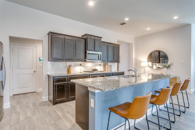 kitchen featuring decorative backsplash, appliances with stainless steel finishes, a breakfast bar, light stone counters, and a sink