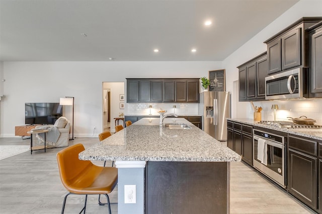 kitchen with light stone counters, light wood-style flooring, appliances with stainless steel finishes, a sink, and an island with sink