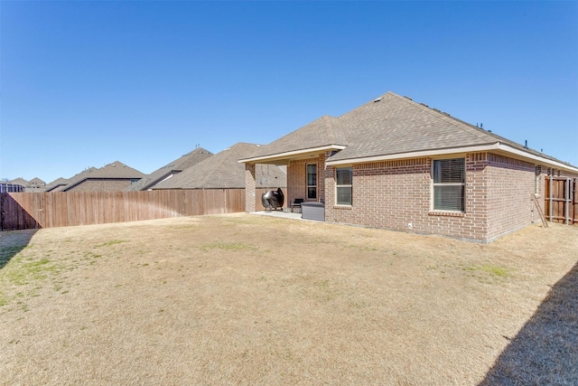 back of property featuring a patio, a fenced backyard, brick siding, a shingled roof, and a lawn