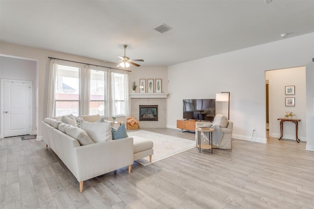 living room featuring baseboards, visible vents, a ceiling fan, a tile fireplace, and light wood-type flooring