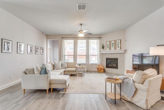 living area featuring visible vents, a tiled fireplace, a ceiling fan, light wood-type flooring, and baseboards