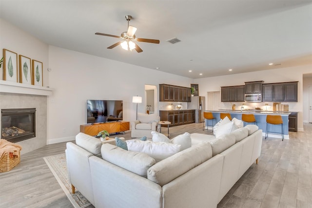 living area featuring ceiling fan, a tile fireplace, recessed lighting, visible vents, and light wood-type flooring