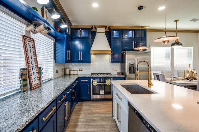 kitchen featuring crown molding, blue cabinetry, stainless steel appliances, a sink, and premium range hood