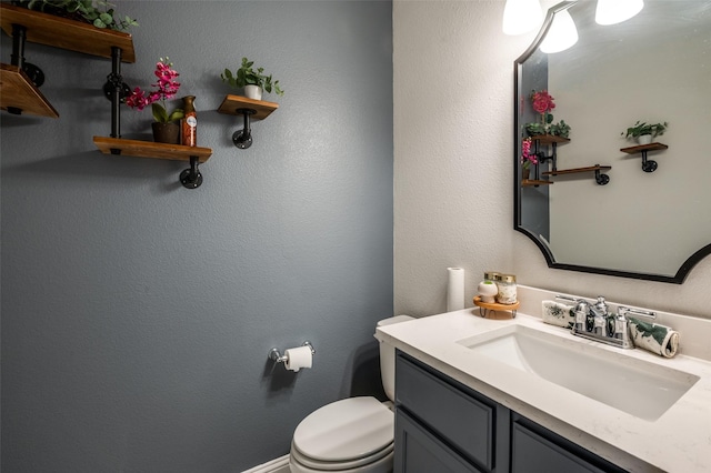 bathroom with a textured wall, vanity, and toilet