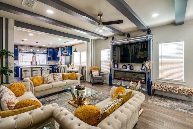 living room with a glass covered fireplace, visible vents, beamed ceiling, and wood finished floors