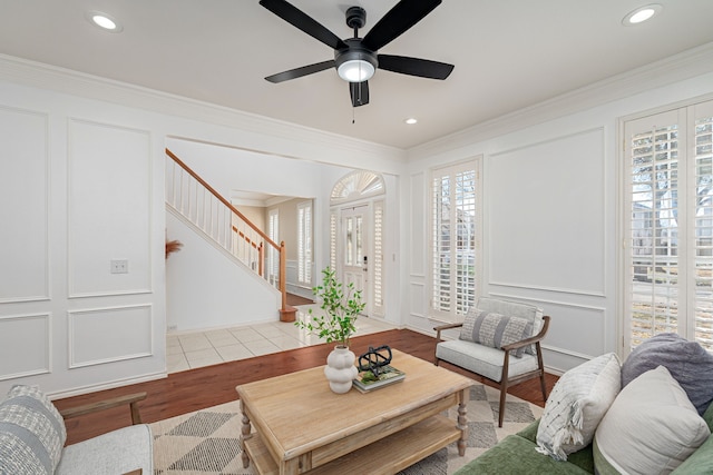 living area with wood finished floors, stairs, crown molding, a decorative wall, and recessed lighting