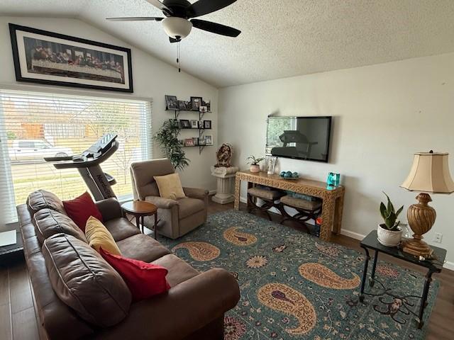 living room featuring a ceiling fan, vaulted ceiling, a textured ceiling, wood finished floors, and baseboards