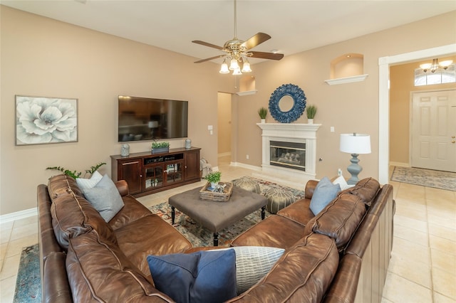 living area with light tile patterned floors, ceiling fan with notable chandelier, a glass covered fireplace, and baseboards