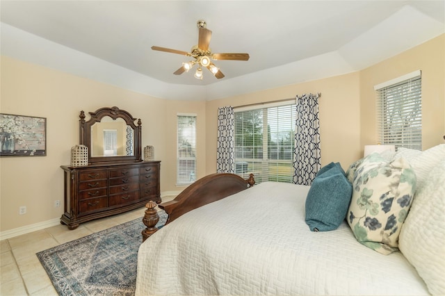 tiled bedroom featuring a ceiling fan, a tray ceiling, and baseboards