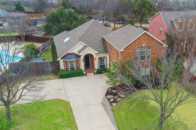 traditional-style home with a shingled roof, a front yard, fence, and brick siding