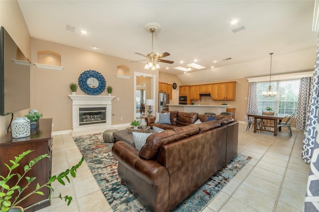 living room featuring light tile patterned floors, lofted ceiling, ceiling fan with notable chandelier, baseboards, and a glass covered fireplace