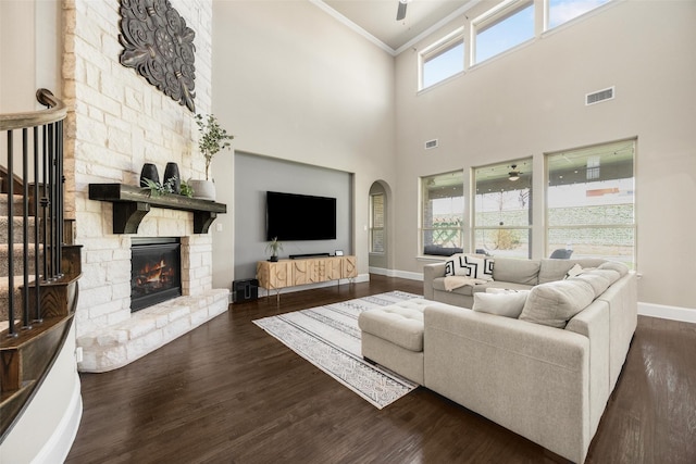 living room featuring baseboards, visible vents, dark wood-type flooring, crown molding, and a stone fireplace