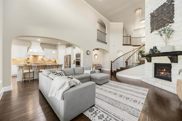 living room with baseboards, arched walkways, a towering ceiling, dark wood-style floors, and a fireplace