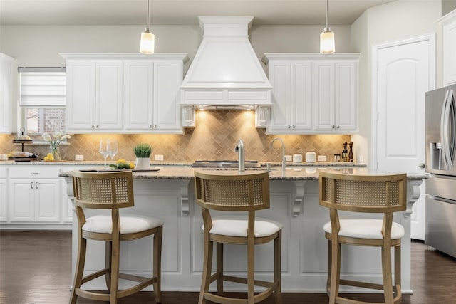 kitchen with white cabinets, custom exhaust hood, stainless steel refrigerator with ice dispenser, and decorative backsplash