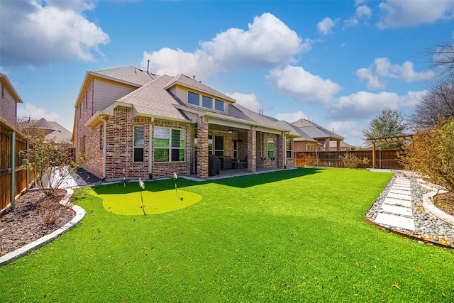 rear view of property with a patio, a fenced backyard, roof with shingles, a yard, and brick siding