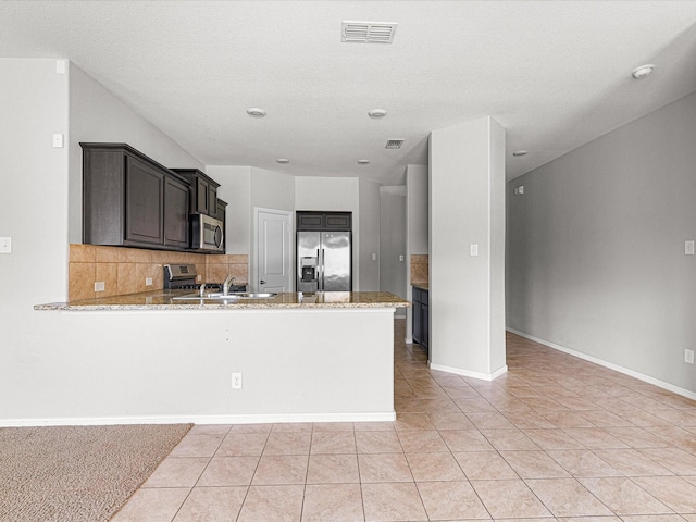 kitchen with stainless steel appliances, visible vents, backsplash, light stone countertops, and a peninsula