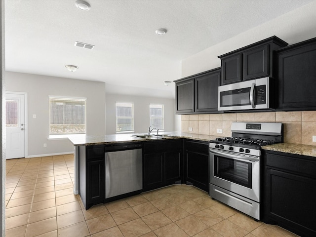 kitchen with visible vents, appliances with stainless steel finishes, backsplash, dark cabinets, and a sink