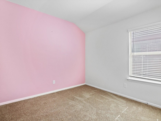 carpeted spare room featuring baseboards and vaulted ceiling