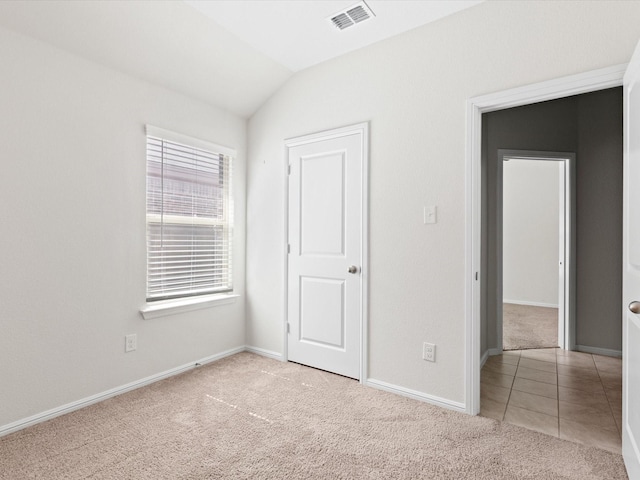 unfurnished bedroom with lofted ceiling, tile patterned flooring, carpet floors, visible vents, and baseboards