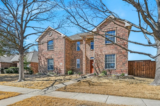 traditional-style home featuring fence, a front lawn, and brick siding