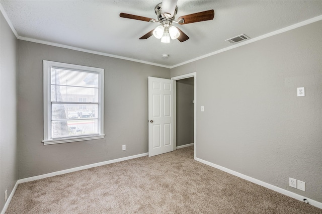 carpeted empty room with baseboards, ceiling fan, visible vents, and crown molding