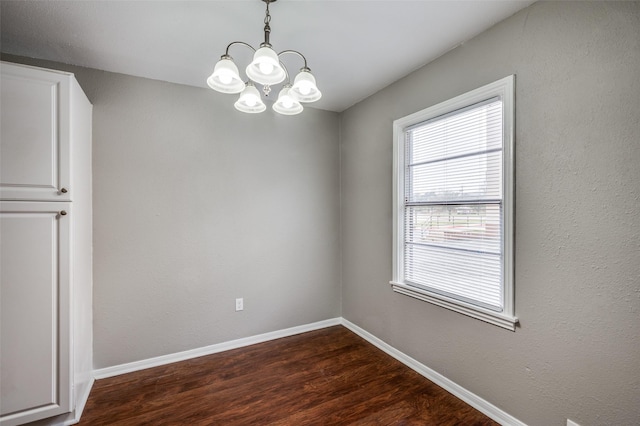 unfurnished dining area with dark wood finished floors, baseboards, and an inviting chandelier