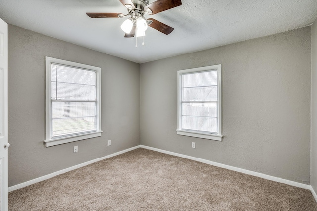 carpeted empty room with a textured wall, a ceiling fan, and baseboards