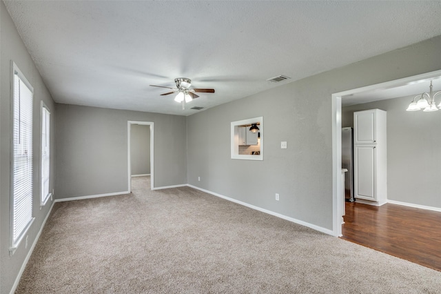 spare room featuring dark colored carpet, visible vents, baseboards, and ceiling fan with notable chandelier