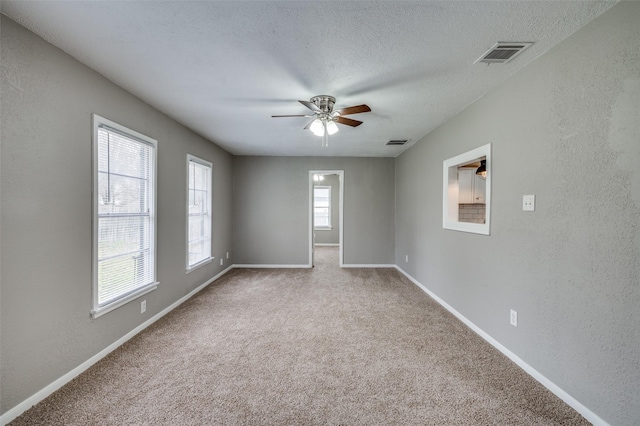 carpeted empty room featuring visible vents, a textured wall, and a textured ceiling