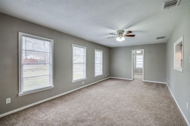 carpeted empty room featuring a textured ceiling, ceiling fan, visible vents, and baseboards