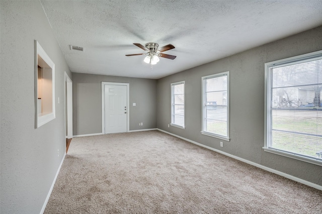 carpeted spare room with a textured ceiling, a textured wall, ceiling fan, visible vents, and baseboards