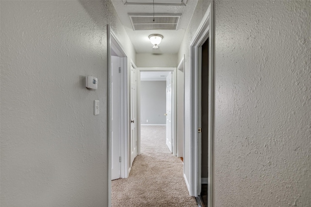 corridor featuring carpet, visible vents, attic access, and a textured wall