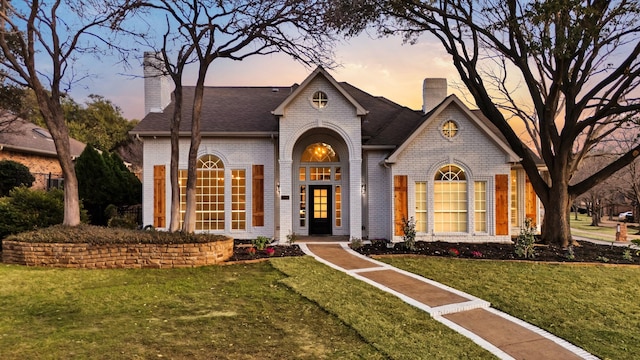 view of front facade featuring a front yard, a shingled roof, a chimney, and brick siding