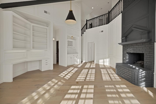 unfurnished living room featuring built in shelves, light wood-style flooring, a decorative wall, visible vents, and a brick fireplace