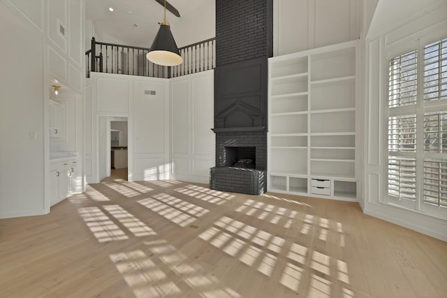 unfurnished living room featuring visible vents, a fireplace, light wood-style flooring, and a decorative wall