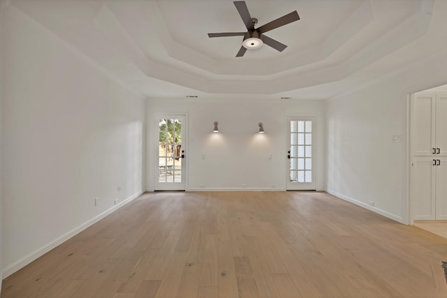 unfurnished room featuring a tray ceiling, a healthy amount of sunlight, and light wood-style flooring