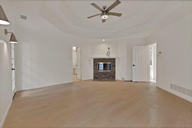 unfurnished living room featuring a fireplace, a raised ceiling, visible vents, and light wood-style floors