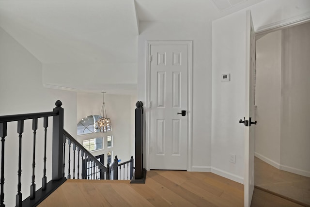 hallway with a chandelier, wood finished floors, visible vents, an upstairs landing, and baseboards