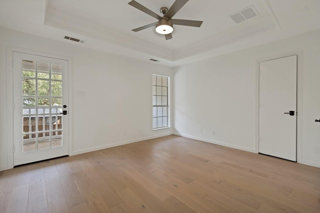 spare room featuring plenty of natural light, visible vents, a tray ceiling, and light wood-style flooring