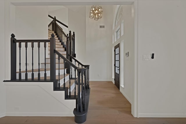 foyer entrance featuring baseboards, visible vents, wood finished floors, stairs, and a chandelier