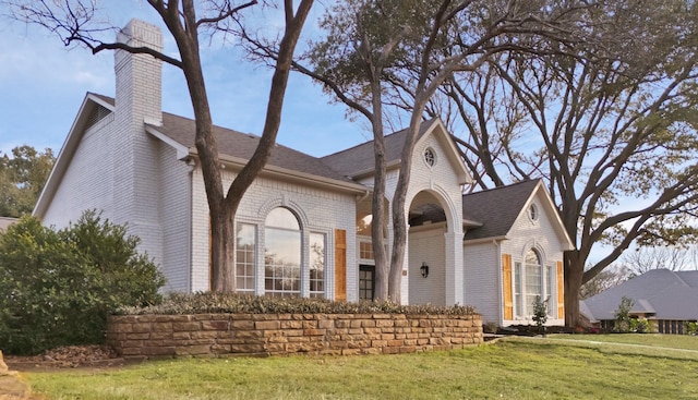 view of front of house featuring brick siding, a front lawn, a chimney, and a shingled roof