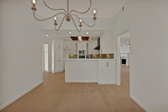 kitchen with light wood-style floors, stainless steel microwave, wall chimney range hood, and white cabinetry