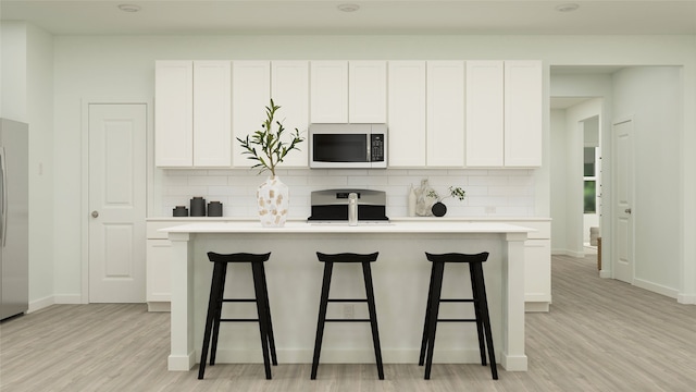 kitchen featuring a kitchen island with sink, stove, white cabinets, backsplash, and stainless steel microwave