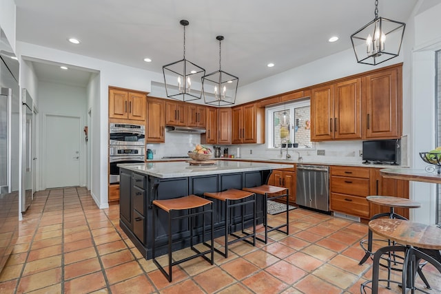 kitchen featuring appliances with stainless steel finishes, brown cabinetry, a sink, a kitchen island, and a kitchen bar