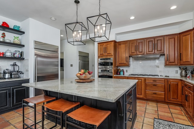 kitchen with under cabinet range hood, stainless steel appliances, a kitchen island, light stone countertops, and open shelves