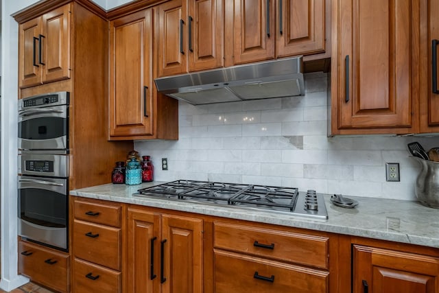 kitchen with appliances with stainless steel finishes, brown cabinetry, decorative backsplash, and under cabinet range hood