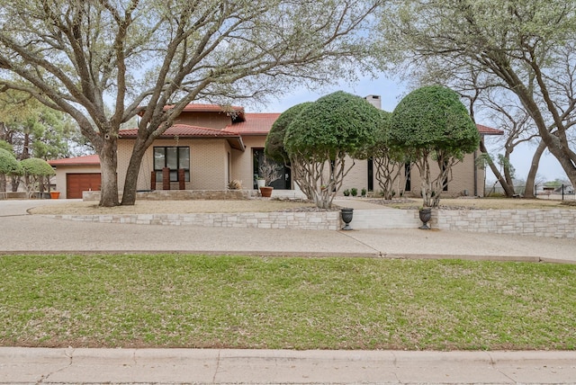 view of front of home featuring a garage, brick siding, a tile roof, and a front yard