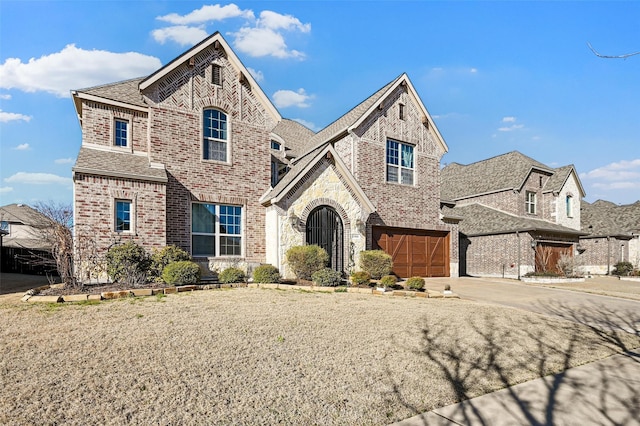 french provincial home with brick siding, roof with shingles, concrete driveway, a garage, and stone siding