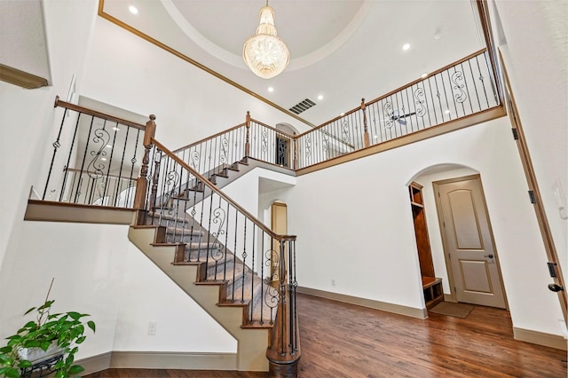 stairs with a towering ceiling, an inviting chandelier, wood finished floors, visible vents, and arched walkways